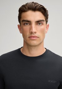 Zwarte lange mouwen shirt met een ronde hals, gemaakt van een gladde stof. Heeft een subtiele verhoogde logo aan de linkerzijde.