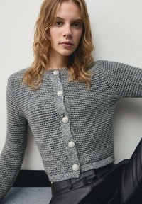 Cardigan gri tricotat cu un model texturat, având șase butoane decorative pe față și manșete și tiv ribbate.