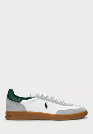 Białe i szare niskie trampki z gumową podeszwą, zielonym kołnierzem przy pięcie, białymi sznurowadłami i czarnym logo Polo Ralph Lauren z boku.