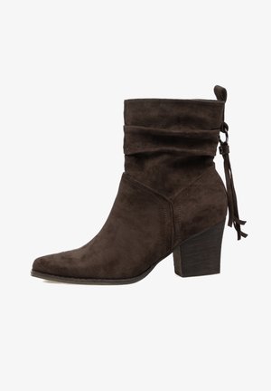 Bota corta de ante marrón con parte superior caída, puntera puntiaguda y tacón apilado. Cuenta con un lazo decorativo en la parte trasera.