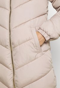 Chaqueta acolchada de color beige claro con cierre de cremallera, diseño acolchado con patrones en forma de chevrón y puños elastizados. Incluye bolsillos laterales.