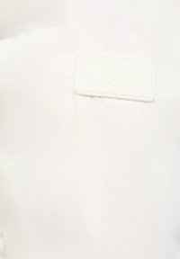 Gros plan sur un tissu blanc avec une pièce rectangulaire texturée embossée du mot "MUSTANG" cousue dessus.