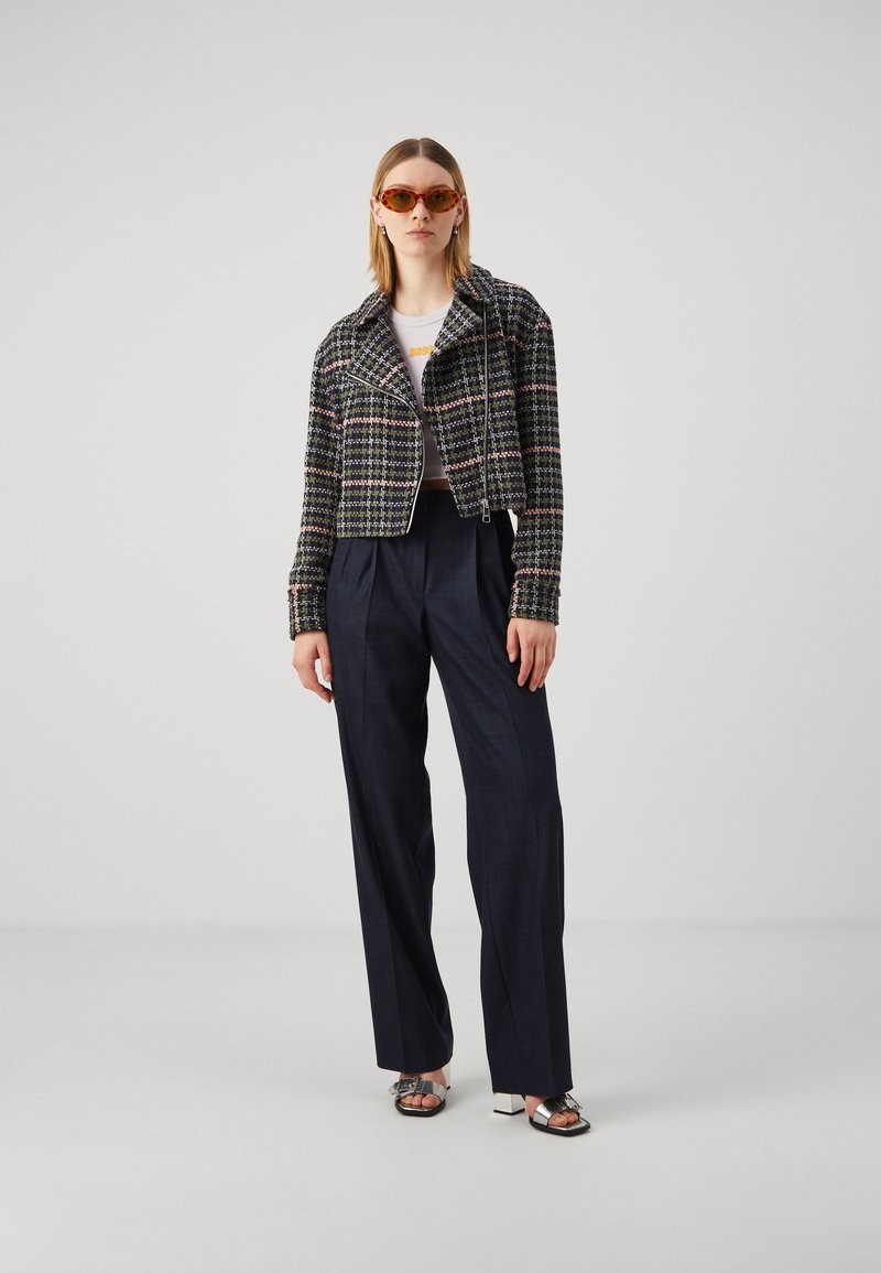 Kobieta nosząca pomarańczowe okulary w kocim kształcie, skróconą marynarkę w kratę, białą skróconą bluzkę, szerokie granatowe spodnie i metaliczne sandały na obcasie.