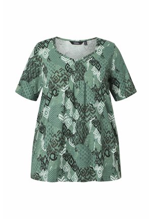 Zielona bluzka z krótkim rękawem, z okrągłym dekoltem i abstrakcyjnymi czarno-białymi geometrycznymi wzorami na całej tkaninie.