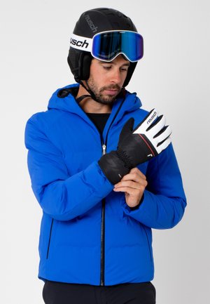 Blue puffer jacket with a hood, worn over a black base layer. Black and white gloves with red accents. Snow helmet and ski goggles.