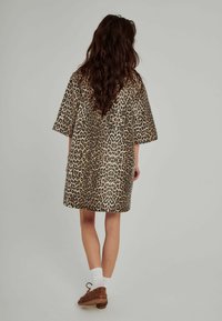 Kleid mit Leopardenmuster, kurze Ärmel, lockere Passform, knielang, der Stoff hat eine glatte Textur. Kombiniert mit braunen Schnürschuhen und weißen Socken.