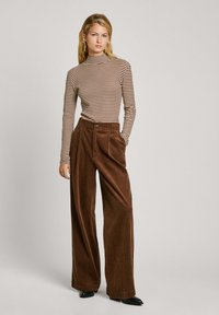 Stripet turtleneck topp i brun og beige, kombinert med brede brune cordbukser med folder og sidelommer. Svarte spisse sko.