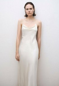Satin, ärmlös maxiklänning i off-white. Har en rak halsringning, figurnära liv och en flödande kjol med en jämn textur.