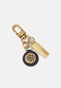 Metalowy brelok z klamrą, z czarnym okrągłym charms jednym, na którym znajduje się wzór kwiatowy oraz złotą zawieszką z napisem "GUESS". Wykonany z teksturowanych i solidnych materiałów.