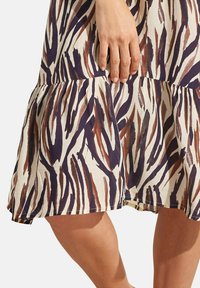Korte mouw jurk in crème met bruine en marineblauwe zebra strepen, met een tiered zoom en een zachte, lichte stoftextuur.