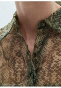 Lekka, przezroczysta bluzka w brązowym kolorze z wzorem węża. Posiada kołnierzyk i zapięcie na guziki. Miękka tekstura i subtelny blask.