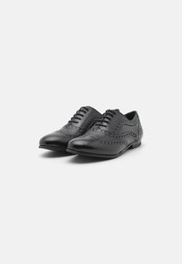 Černé kožené šaty obuv se štíhlým designem, detaily ve stylu wingtip a dekorativní perforace, s hladkým povrchem a zavazováním na tkaničky.