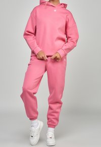 Felpa e pantaloni della tuta rosa realizzati in materiale morbido, con una vestibilità comoda, polsini elasticizzati e un piccolo logo sul capo.