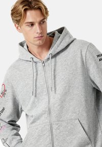 Hall hall lukuga dressipluus, valmistatud pehmest kangast, millel on kapuuts paelaga, ees taskud ja varrukatel trükitud detailid.