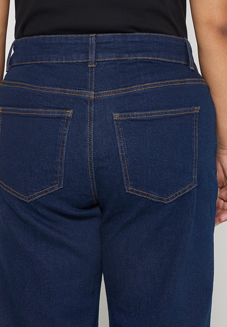 Un jean en denim bleu foncé, avec une texture lisse, une coupe droite, et deux poches arrière avec des détails de surpiqûres orange.