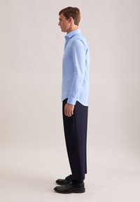 Camicia a maniche lunghe azzurro chiaro con collo a patta, abbinata a pantaloni blu navy scuri e scarpe nere. Tessuto morbido e vestibilità su misura.