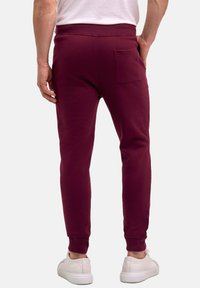 Burgunderfarbene Sweatpants mit passgenauer Schnittführung, elastischem Bund und einer Gesäßtasche. Hergestellt aus weichem Stoff und kombiniert mit weißen Sneakers.