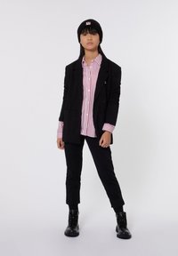 Blazer negro de gran tamaño sobre una camisa a rayas rojas y blancas, combinado con pantalones negros con puños enrollados y botas negras de cordones. Gorro de punto negro.