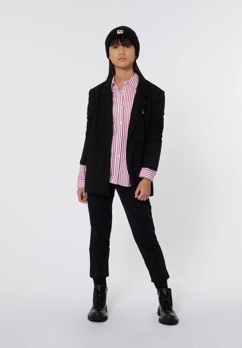 Blazer negro de gran tamaño sobre una camisa a rayas rojas y blancas, combinado con pantalones negros con puños enrollados y botas negras de cordones. Gorro de punto negro.
