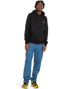 Felpa nera con tasca frontale e cordini, abbinata a jeans in denim blu chiaro. La calzatura presenta un design giallo e nero.