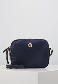 Borsa a tracolla in nylon navy con hardware in tonalità oro, chiusura a zip, tracolla regolabile e logo impresso. Texture liscia e forma rettangolare.