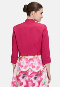 Fuchsia voorgeschreven jas met een hoge hals en driekwart mouwen, gecombineerd met een rok met bloemmotief in roze en groene tinten.