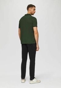 Dunkelgrünes Polohemd mit Kragen, kurzen Ärmeln und schmaler Passform, kombiniert mit schwarzen Hosen und weißen Sneakern. Einfaches Design, keine Muster.