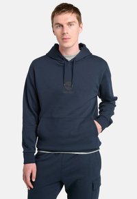 Námořnická modrá mikina s kapucí vyrobená z měkké tkaniny, s klokaní kapsou, nastavovací šňůrkou a logem tištěným na prsou.