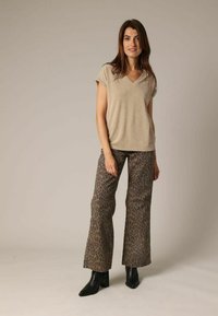 Beige V-hals t-shirt in combinatie met lichtbruine, uitlopende broek met luipaardprint. Zwarte enkellaarsjes maken de outfit compleet. Textuur van de stof zichtbaar.