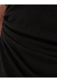 Svart tyg med samlad textur, som visar mjuka draperingslinjer och en slät yta, med fokus på de intrikata veckarna i materialet.