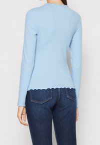 Langärmliges, hellblaues geripptes Oberteil mit einem gewellten Ausschnitt und Saum, kombiniert mit dunkelblauen Jeans.