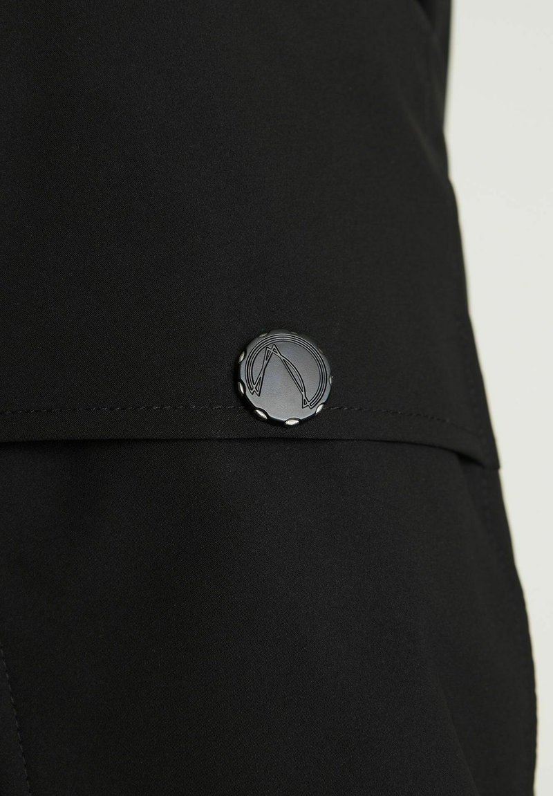 Czarna tkanina o gładkiej fakturze z zaokrąglonym czarnym guzikiem z wygrawerowanym wzorem oraz przeszyciem.