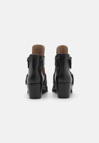 Botines de cuero negro hasta el tobillo con un tacón curvado, parte trasera abierta y una hebilla decorativa en el lateral. Textura suave con un diseño minimalista.