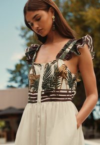 Robe maxi florale avec un imprimé de girafes et de léopards, manches volantées et boutonnage sur le devant. Les couleurs incluent crème, vert et marron.