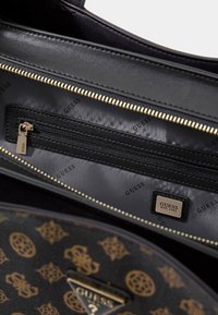 Interieur van een zwarte handtas met gouden ritssluiting en accenten. Voorzien van een stoffen voering met herhalend "GUESS"-logo en een ritssluitingvak voor opslag.