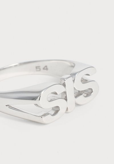 Bague en argent avec des lettres en relief et stylisées formant "sis" et une indication de taille "54" à l'intérieur de l'anneau sur fond blanc.