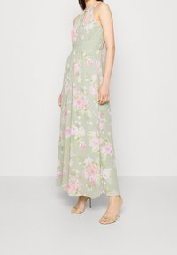 Kukkainen maxi-mekko vaaleanvihreänä, jossa on vaaleanpunaisia ruusukuoseja. Kaula-aukon malli, jossa on kapea vyötärö ja laskostettu hame. Yhdistetty vihreisiin korkokengiin.