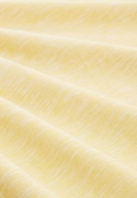 Textil de color amarillo claro con una textura suave y lisa, que presenta patrones de olas sutiles. La tela parece ligera y finamente tejida.