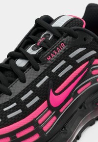 Zapatilla deportiva negra y rosa con materiales de malla y goma, que presenta una destacada marca Max Air, cordones en tono y acentos reflectantes.