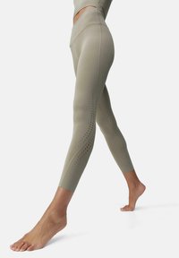 Olijfgroene leggings met een hoge taille, een slank ontwerp, een gestructureerde stof en decoratieve geperforeerde details langs de buitenkant van de benen.