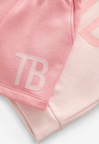 Komadi roza pamučnog duksera u različitim nijansama; jedan ima teksturirani logo "TB" u svijetlo roza boji. Mekana tkanina, detalji od rebrastog materijala na rukavima.