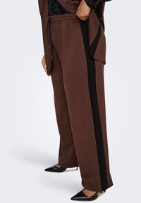 Brown wide-leg pants with black side stripes, made from soft fabric. Features an adjustable waistband and a relaxed fit, paired with black heels.
