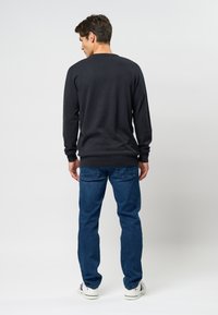 Navy gebreide trui met lange mouwen, geribbelde manchetten en tailleband, gecombineerd met blauwe jeans en witte sneakers met kleuraccenten.