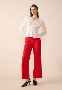 Hvit teksturert bluse med volangdetaljer, kombinert med knallrøde vide bukser og svarte hæl-mules. Enkel, elegant design.