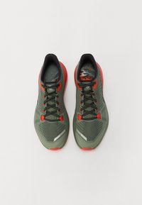 Chaussures de sport vertes et rouges avec une tige en maille, des lacets noirs et une semelle texturée. Présente des accents réfléchissants et une semelle intérieure à motifs.
