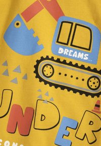 Geel stof met speelse graphics, waaronder een blauwe vrachtwagen, een rode graafmachine en verschillende vormen. De tekst luidt "DREAMS..." en "UNDER."