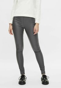 Graue, enganliegende Leggings aus einem glatten, elastischen Material. Abgerundet mit einem eleganten Look, kombiniert mit schwarzen Schnürschuhen.