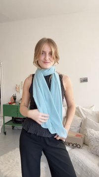 Ανοιχτό μπλε scarf τοποθετημένο γύρω από τον λαιμό πάνω από μία μαύρη υφασμάτινη μπλούζα. Διαθέτει μαλακό, ρευστό ύφασμα με απαλό φινίρισμα και χωρίς ορατά σχέδια.
