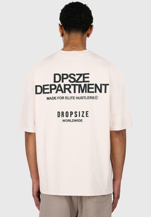 T-shirt beige clair à manches courtes, avec un texte noir en gras au dos : "DPSZE DEPARTMENT," "FAIT POUR LES HUSTLERS ÉLITES," et "DROPSIZE WORLDWIDE."