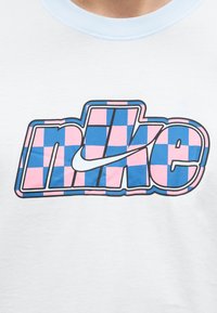 Bela majica z velikim napisom "nike" v modro-roza karo vzorcu in belim Nike logotipom (swoosh) čez črke.